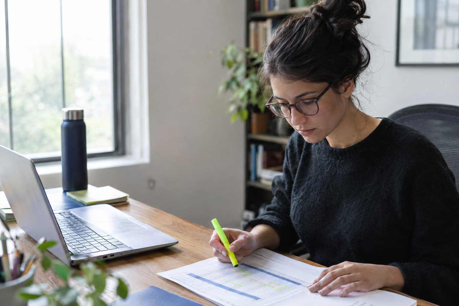 A researcher highlighting a printed table beside a laptop