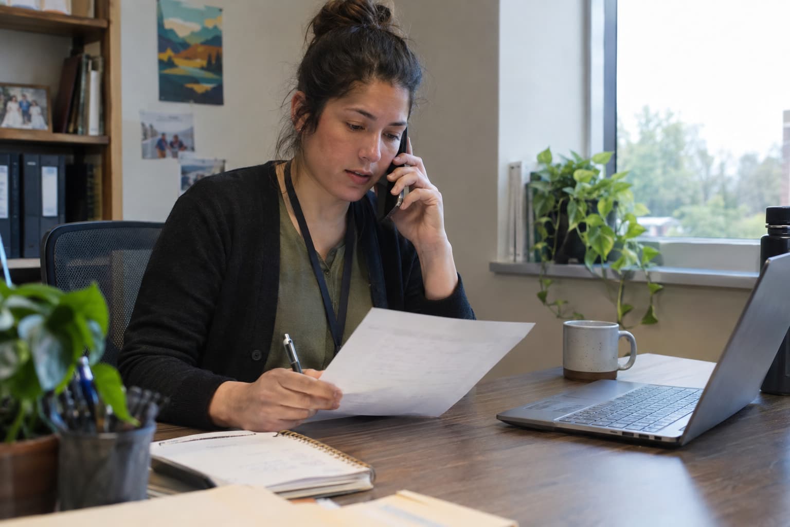 A finance manager on a phone call reading a printed vendor quote with a pen in hand