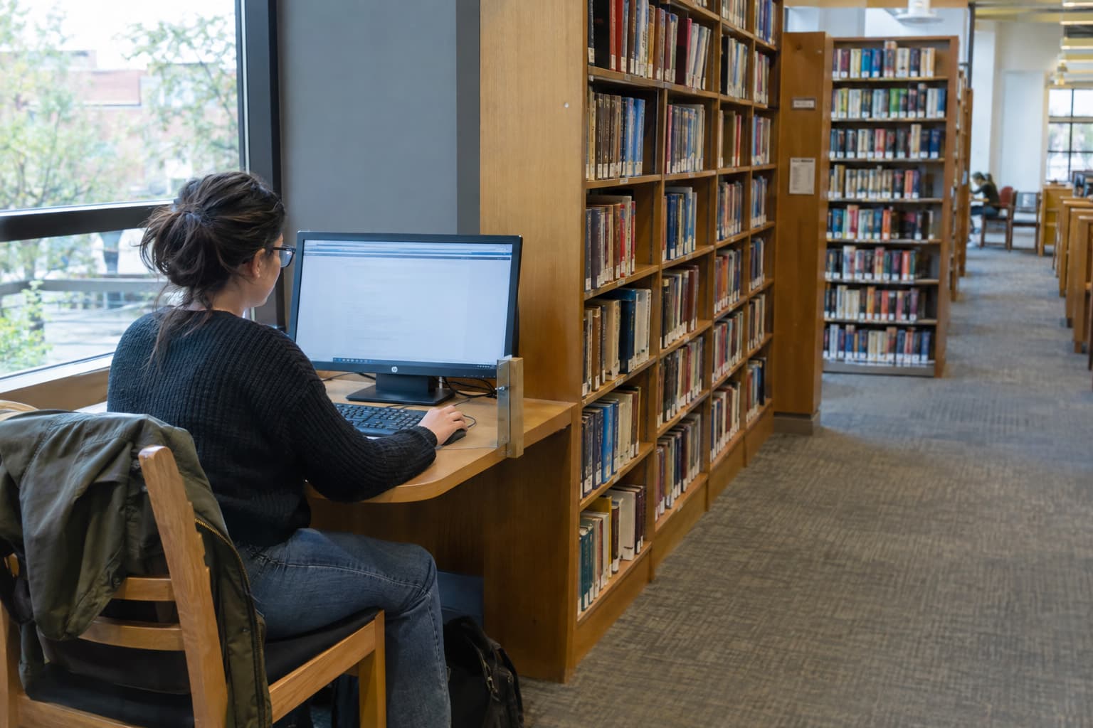 A person using a public library computer near tall bookshelves
