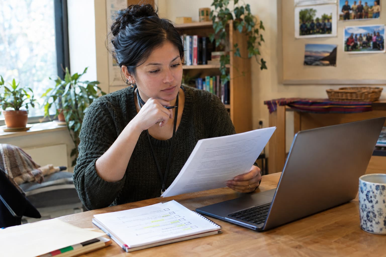 A staff member reading printed pages beside a laptop and a marked-up checklist