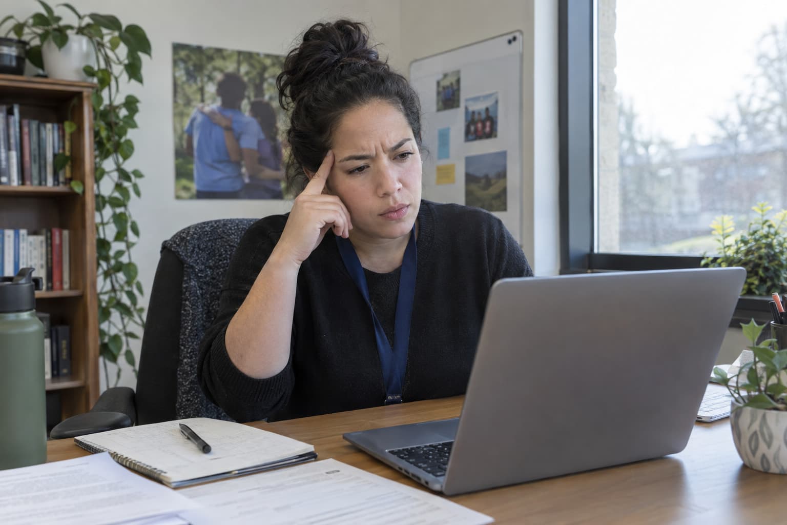 A staff member at a desk looking at a laptop screen with a puzzled expression