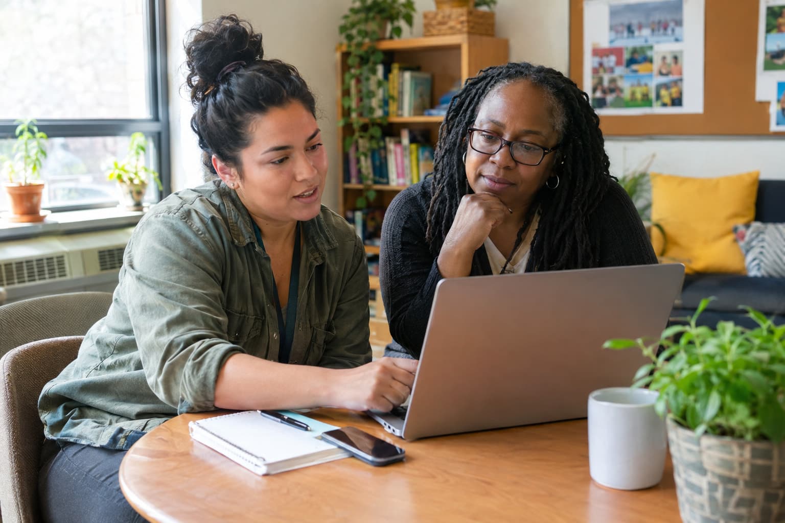Two staff members at a small table comparing notes on a laptop
