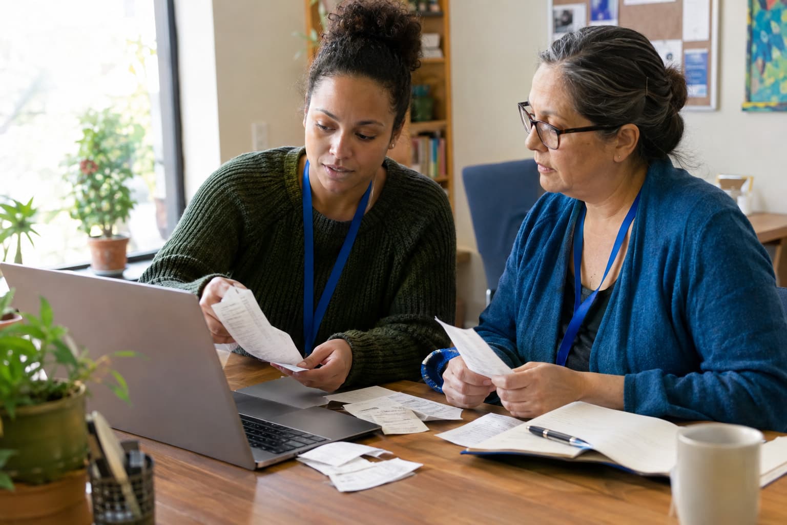 Two staff members comparing printed receipts against a laptop at a shared desk