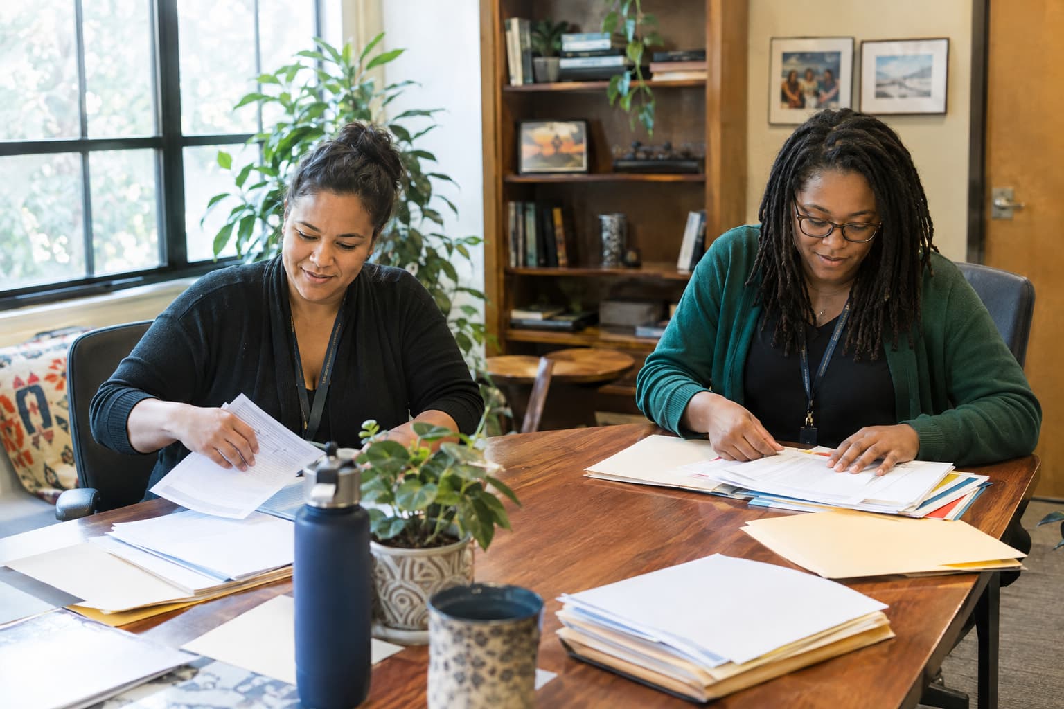 Two staff members sorting printed documents and folders across a conference table