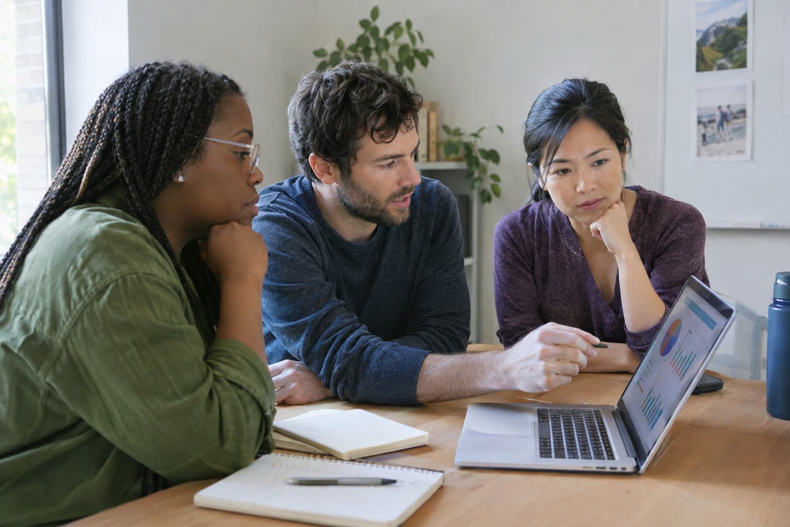 Three team members reviewing charts on a laptop in a small meeting room