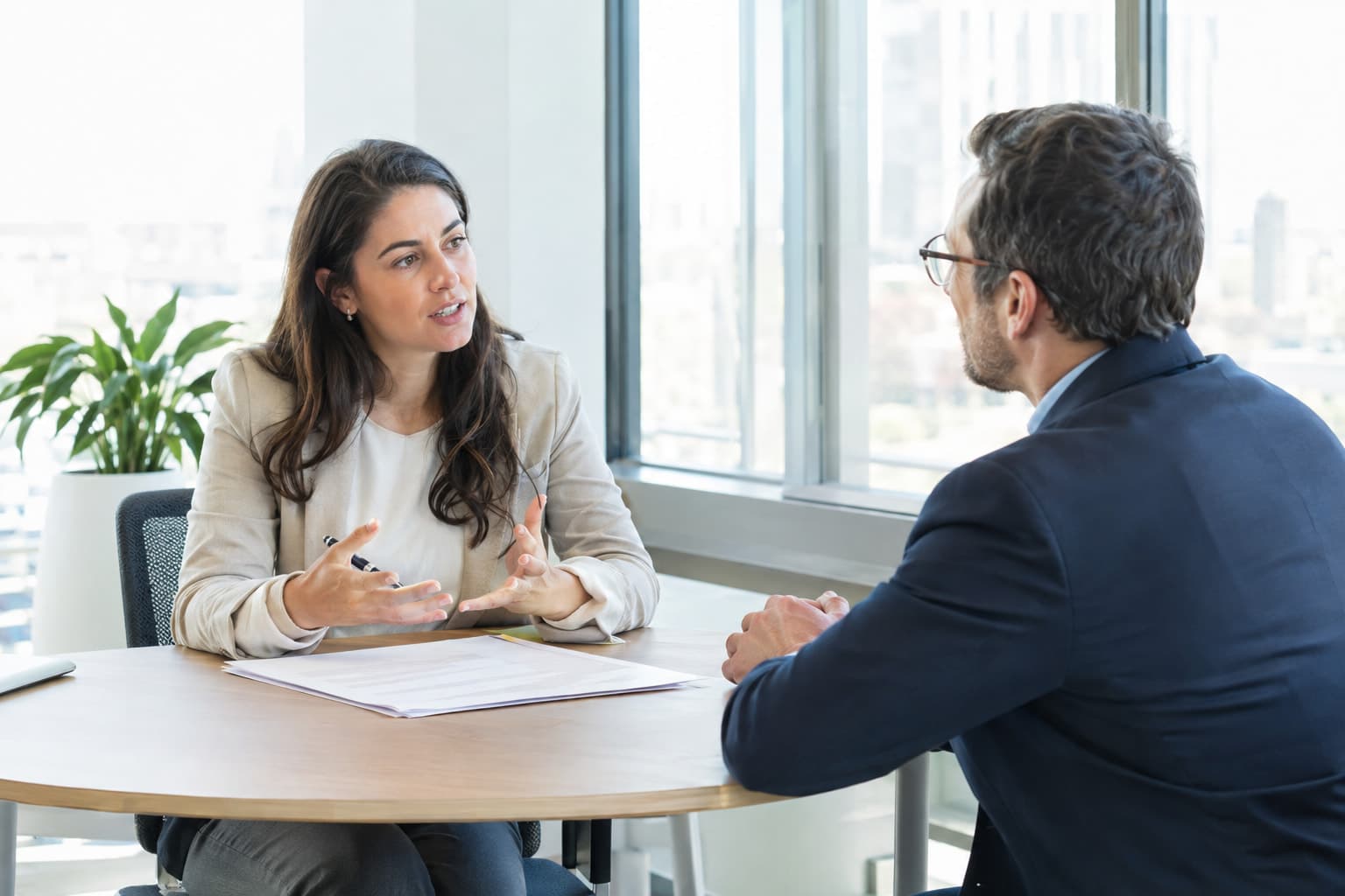 Two people talking across a small meeting table with papers between them
