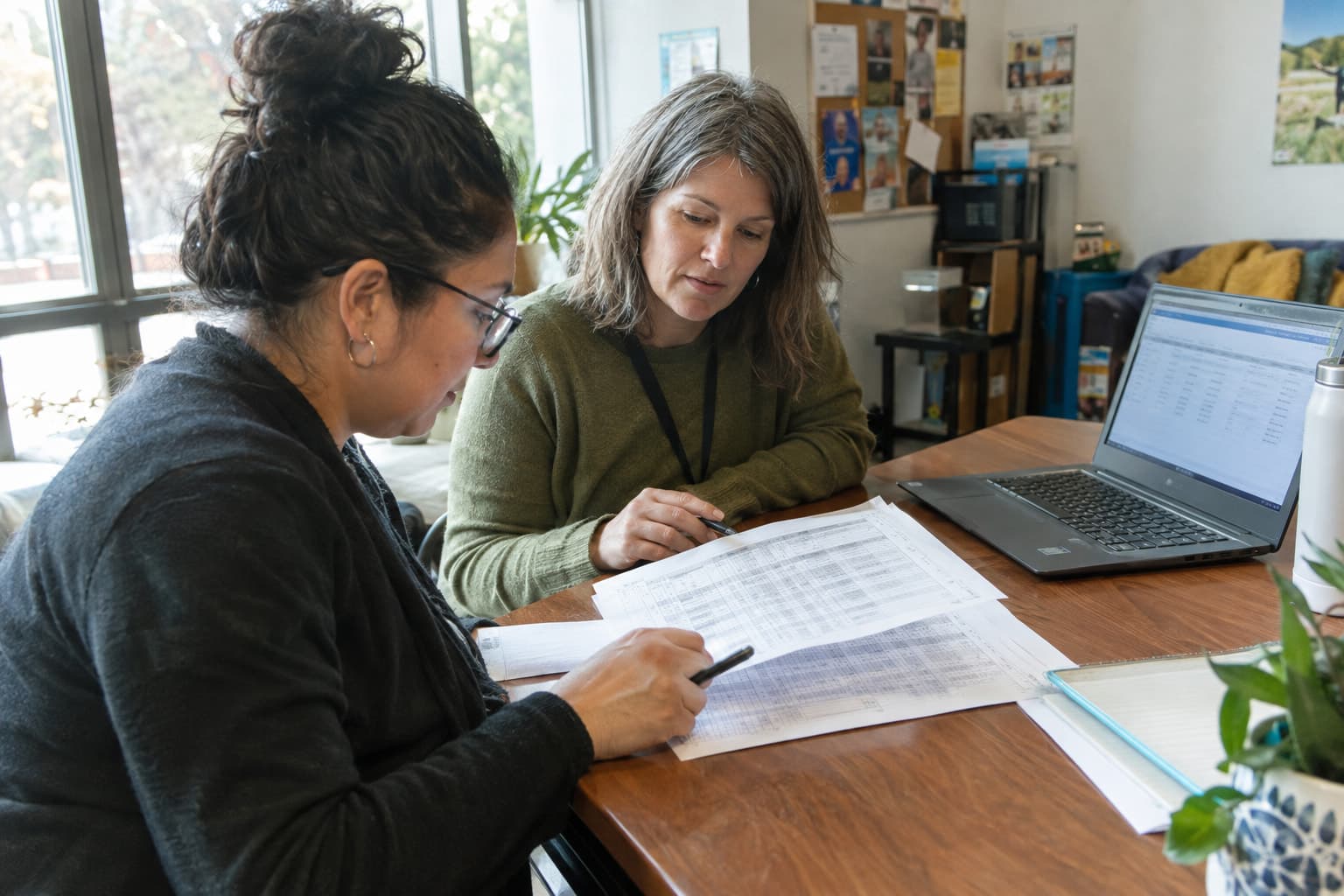 Staff reviewing printed sheets beside a laptop in a community office