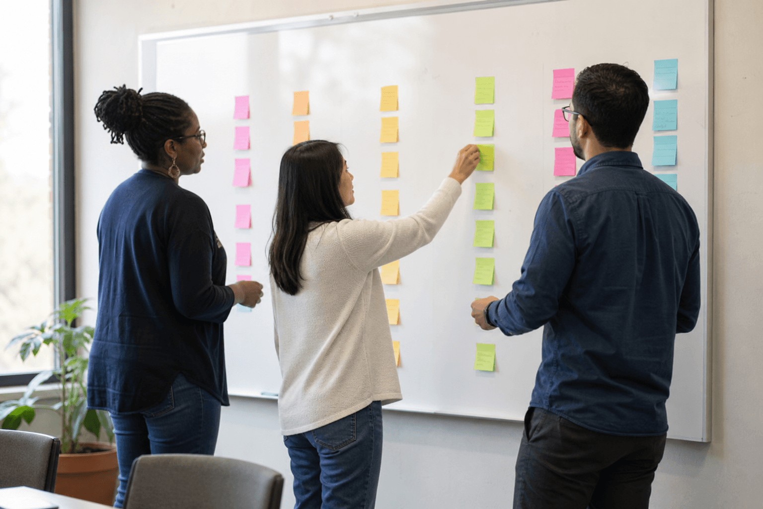 Nonprofit staff arranging sticky notes into logic model columns on a whiteboard