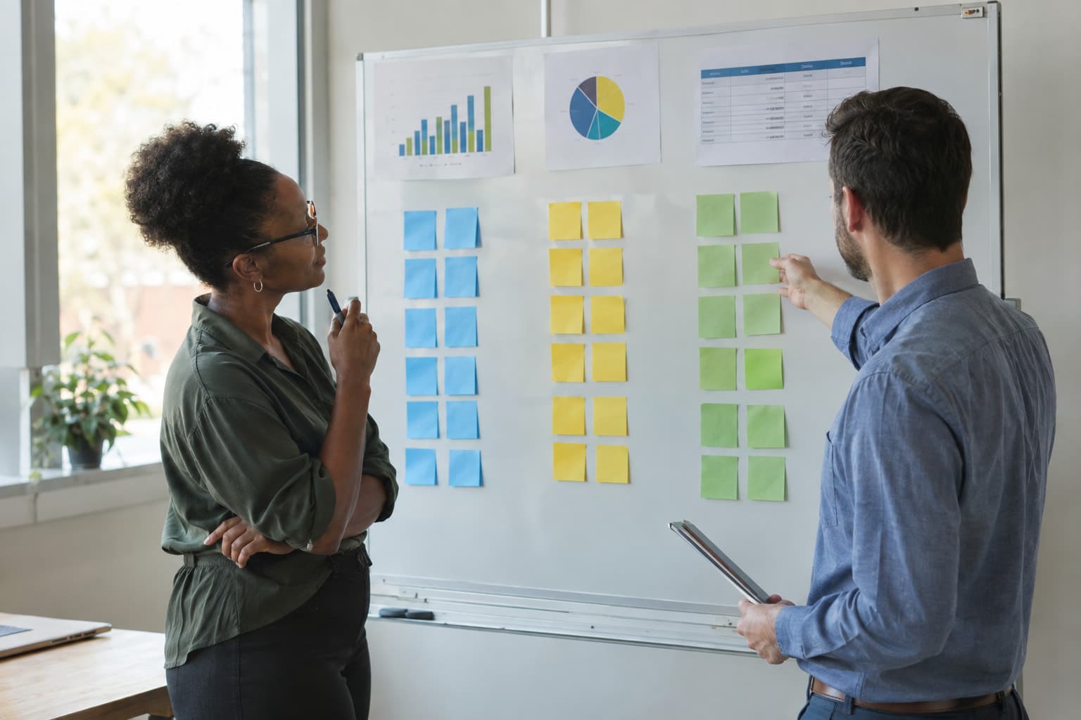 Two staff members at a whiteboard covered with three columns of square notes