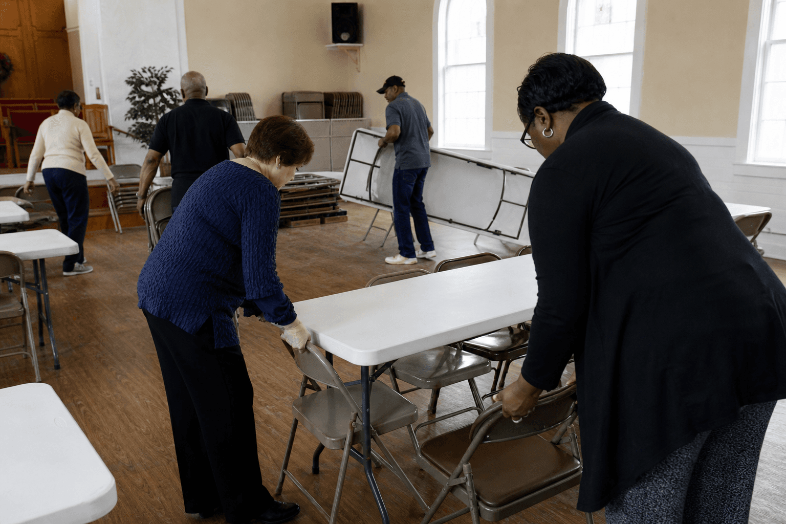 Volunteers setting up folding tables in a church fellowship hall before a community program
