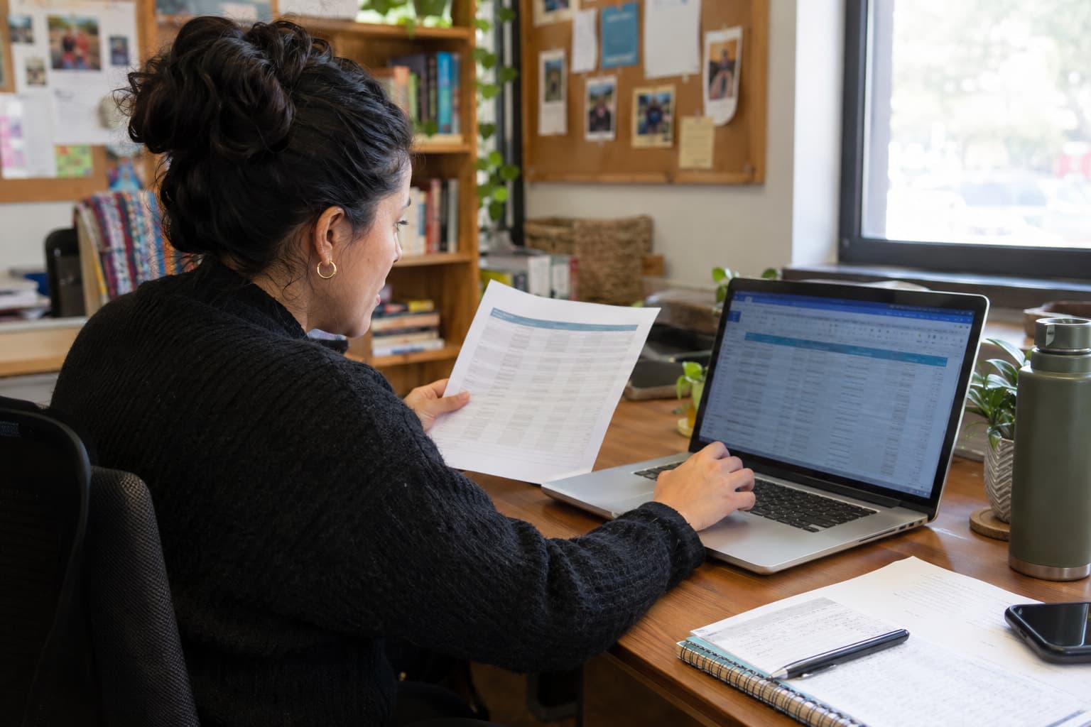 A staff member comparing a printed list against a laptop screen at a desk