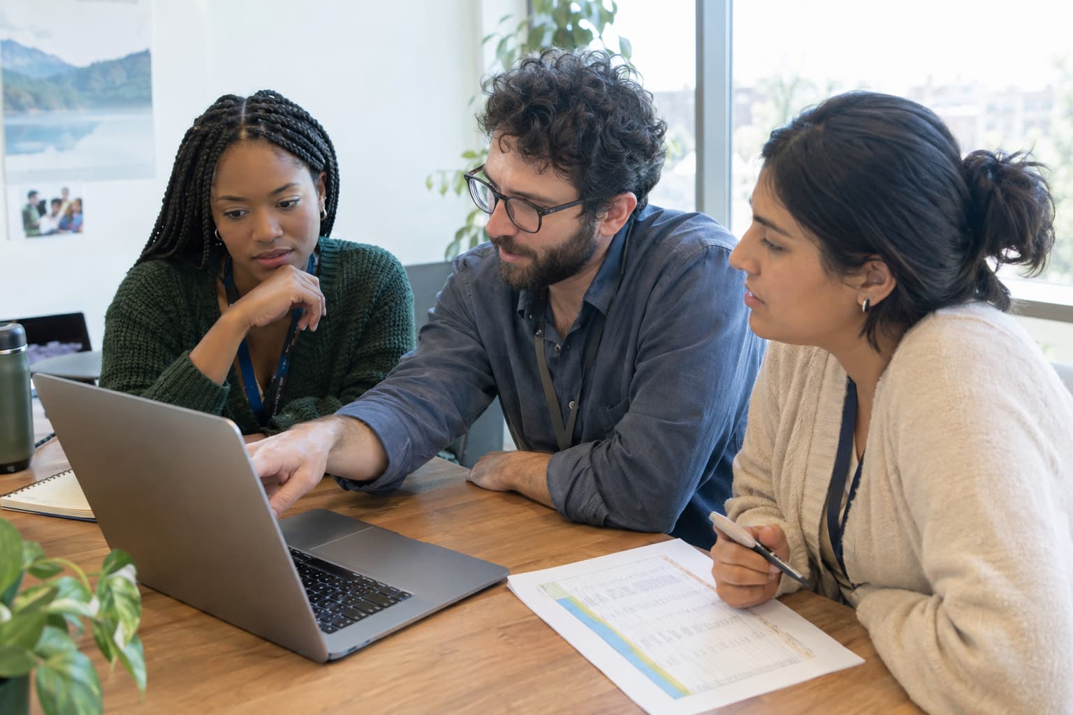 Three staff members around a laptop and a printed spreadsheet in a bright meeting room