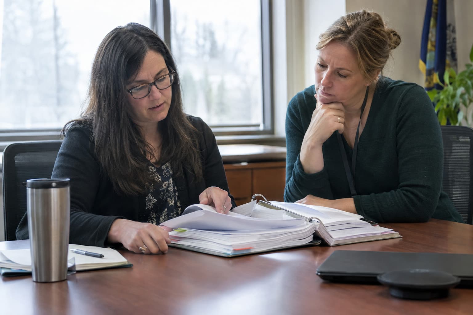 Two municipal staff members reviewing a binder of contracts at a meeting table